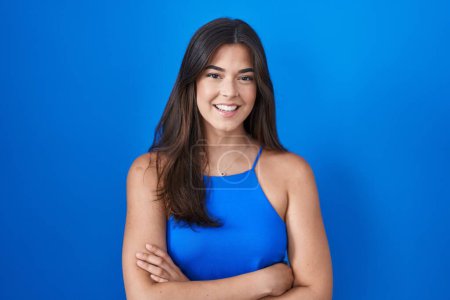 Photo for Hispanic woman standing over blue background happy face smiling with crossed arms looking at the camera. positive person. - Royalty Free Image