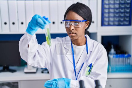 Téléchargez les photos : Young african american woman scientist holding test tubes at laboratory - en image libre de droit