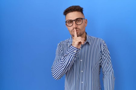 Foto de Hombre hispano con barba usando gafas pidiendo silencio con el dedo en los labios. silencio y concepto secreto. - Imagen libre de derechos