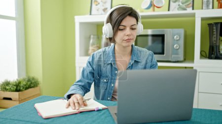 Photo for Young caucasian woman using laptop writing on notebook at home - Royalty Free Image
