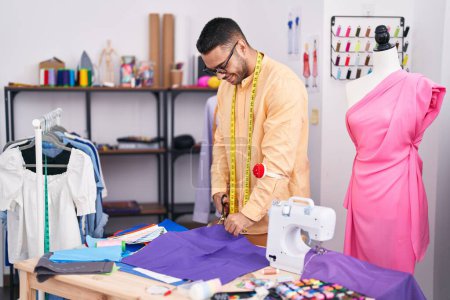 Téléchargez les photos : Jeune homme hispanique tailleur souriant tissu de coupe confiant à la boutique de tailleur - en image libre de droit