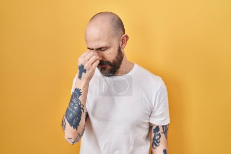 Photo for Young hispanic man with tattoos standing over yellow background tired rubbing nose and eyes feeling fatigue and headache. stress and frustration concept. - Royalty Free Image