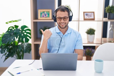 Photo for Hispanic man working using computer laptop wearing headphones pointing thumb up to the side smiling happy with open mouth - Royalty Free Image