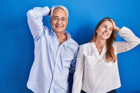 Photo for Middle age hispanic couple standing over blue background smiling confident touching hair with hand up gesture, posing attractive and fashionable - Royalty Free Image