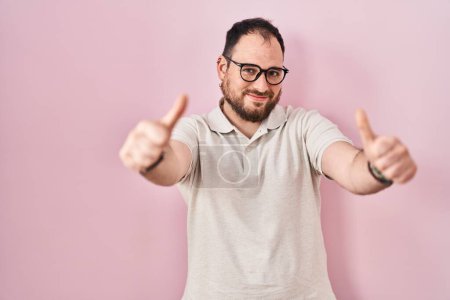 Photo for Plus size hispanic man with beard standing over pink background approving doing positive gesture with hand, thumbs up smiling and happy for success. winner gesture. - Royalty Free Image