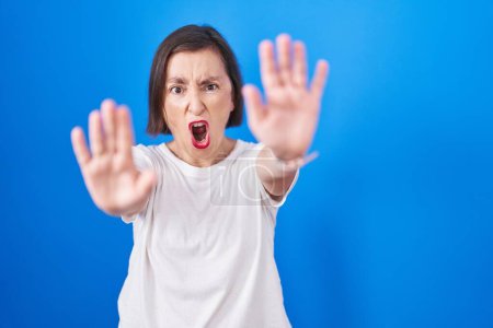 Téléchargez les photos : Middle age hispanic woman standing over blue background doing stop gesture with hands palms, angry and frustration expression - en image libre de droit