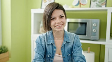 Téléchargez les photos : Jeune femme caucasienne souriante confiante assise sur la table à la maison - en image libre de droit