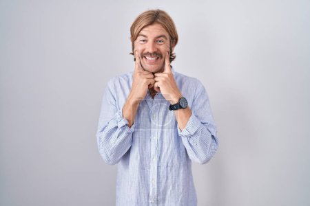 Foto de Hombre caucásico con bigote de pie sobre fondo blanco sonriendo con la boca abierta, los dedos señalando y forzando sonrisa alegre - Imagen libre de derechos