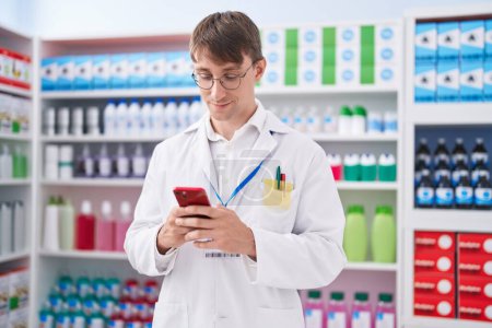 Téléchargez les photos : Jeune pharmacien homme caucasien utilisant un smartphone travaillant à la pharmacie - en image libre de droit