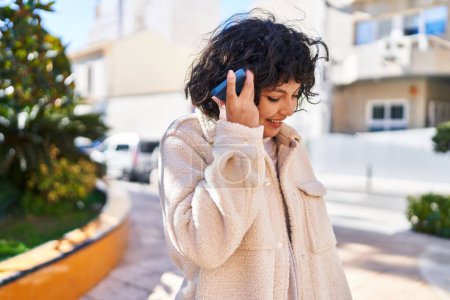 Téléchargez les photos : Jeune belle femme hispanique souriant confiant écoute message audio par le smartphone au parc - en image libre de droit