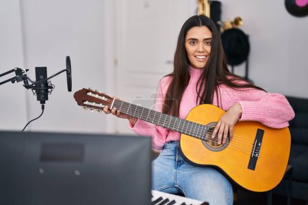 Photo for Young hispanic woman musician playing guitar at music studio - Royalty Free Image