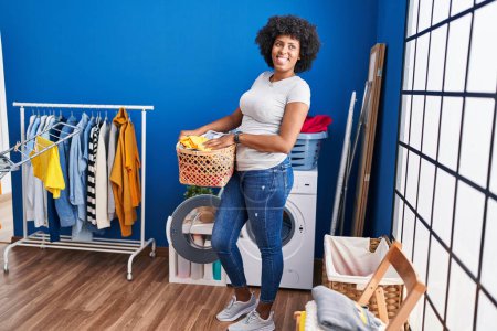 Foto de African american woman smiling confident holding basket with clothes at laundry room - Imagen libre de derechos