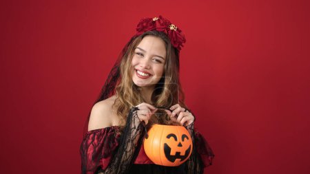 Téléchargez les photos : Jeune belle femme hispanique portant katrina costume tenant panier de citrouille halloween sur fond rouge isolé - en image libre de droit