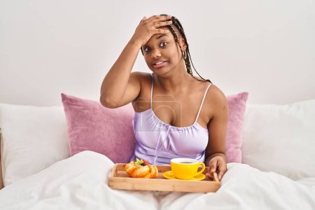 Téléchargez les photos : Femme afro-américaine avec des tresses tenant plateau avec de la nourriture pour le petit déjeuner dans le lit stressé et frustré avec la main sur la tête, visage surpris et en colère - en image libre de droit