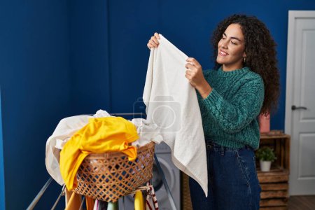 Photo for Young beautiful hispanic woman smiling confident hanging clothes on clothesline at laundry room - Royalty Free Image