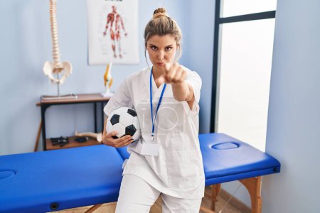 Téléchargez les photos : Jeune femme travaillant à la clinique de thérapie de football pointant du doigt la caméra et à vous, geste confiant regardant sérieux - en image libre de droit