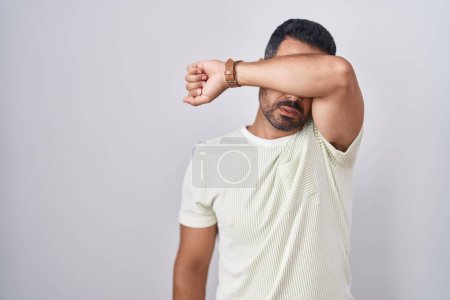 Téléchargez les photos : Homme hispanique avec la barbe debout sur fond isolé couvrant les yeux avec le bras, l'air grave et triste. concept de non-visibilité, de dissimulation et de rejet - en image libre de droit