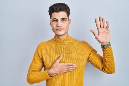 Photo for Young hispanic man standing over blue background swearing with hand on chest and open palm, making a loyalty promise oath - Royalty Free Image