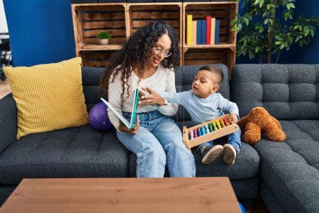 Photo for Mother and son reading book sitting on sofa at home - Royalty Free Image