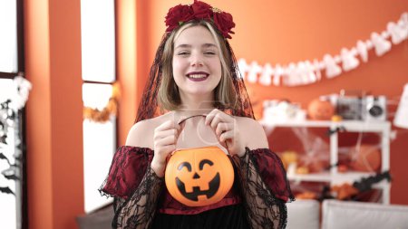 Téléchargez les photos : Young blonde woman wearing katrina costume holding halloween pumpkin basket at home - en image libre de droit