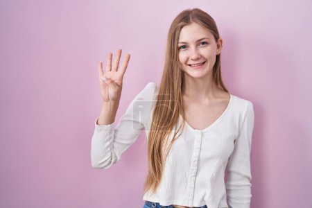 Foto de Young caucasian woman standing over pink background showing and pointing up with fingers number four while smiling confident and happy. - Imagen libre de derechos