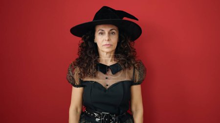 Foto de Middle age hispanic woman wearing witch costume having halloween party over isolated red background - Imagen libre de derechos