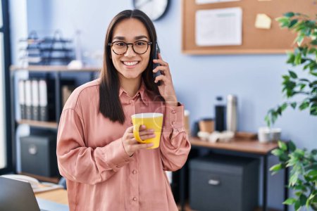Téléchargez les photos : Jeune ouvrière hispanique parlant sur smartphone buvant du café au bureau - en image libre de droit