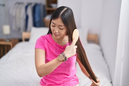 Photo for Chinese woman combing hair sitting on bed at bedroom - Royalty Free Image