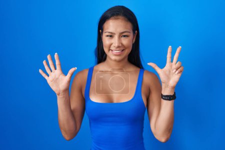 Photo for Hispanic woman standing over blue background showing and pointing up with fingers number eight while smiling confident and happy. - Royalty Free Image