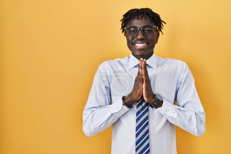 Photo for African man with dreadlocks standing over yellow background praying with hands together asking for forgiveness smiling confident. - Royalty Free Image
