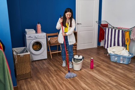 Photo for Young hispanic woman smiling confident washing floor using mop at laundry room - Royalty Free Image