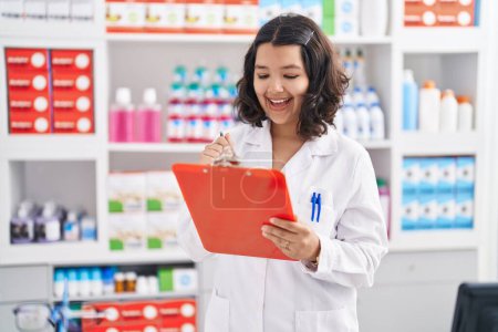 Photo for Young woman pharmacist writing on document at pharmacy - Royalty Free Image