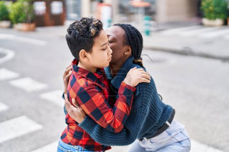 Téléchargez les photos : Afro-américaine mère et fils souriant confiant étreignant l'autre et s'embrassant dans la rue - en image libre de droit