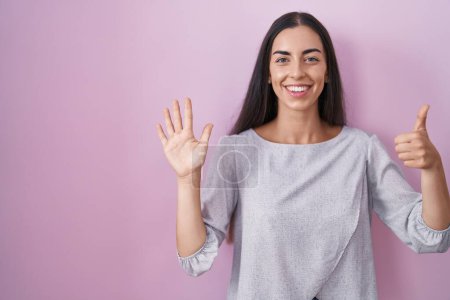 Téléchargez les photos : Young brunette woman standing over pink background showing and pointing up with fingers number six while smiling confident and happy. - en image libre de droit