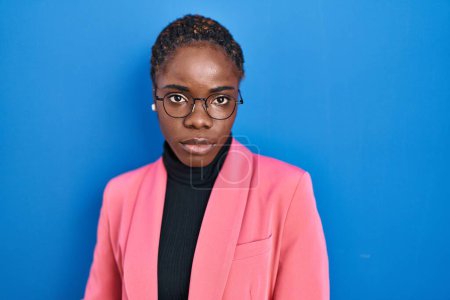 Photo for Beautiful black woman standing over blue background relaxed with serious expression on face. simple and natural looking at the camera. - Royalty Free Image