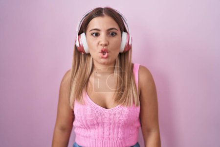 Photo for Young blonde woman listening to music using headphones making fish face with lips, crazy and comical gesture. funny expression. - Royalty Free Image