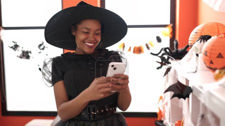 Photo for African american woman wearing witch costume using smartphone at home - Royalty Free Image