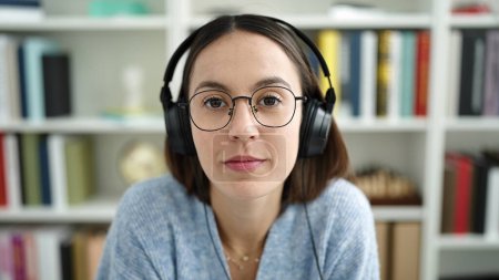 Téléchargez les photos : Jeune belle étudiante hispanique écoutant de la musique avec une expression détendue à la bibliothèque de l'université - en image libre de droit