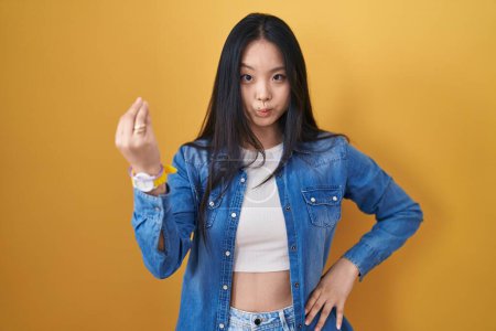Foto de Joven mujer asiática de pie sobre fondo amarillo haciendo gesto italiano con la mano y los dedos expresión confiada - Imagen libre de derechos