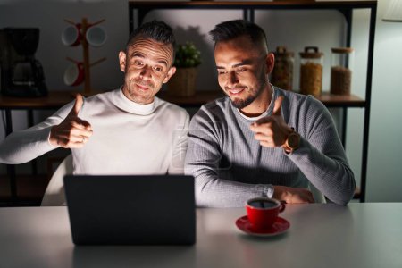 Photo for Homosexual couple using computer laptop pointing fingers to camera with happy and funny face. good energy and vibes. - Royalty Free Image