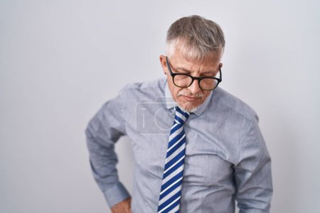 Téléchargez les photos : Homme d'affaires hispanique aux cheveux gris portant des lunettes souffrant de maux de dos, touchant le dos avec la main, douleurs musculaires - en image libre de droit