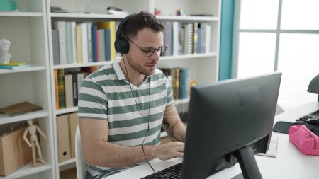 Téléchargez les photos : Young caucasian man using computer wearing headphones at library university - en image libre de droit
