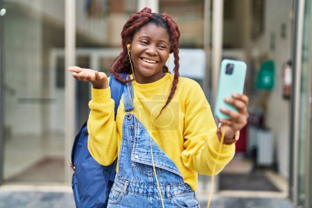 Téléchargez les photos : Femme africaine faisant appel vidéo avec smartphone célébrant la réalisation avec sourire heureux et expression gagnante avec la main levée - en image libre de droit