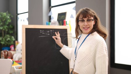 Téléchargez les photos : Jeune femme caucasienne enseignant des mots sur tableau noir à la maternelle - en image libre de droit