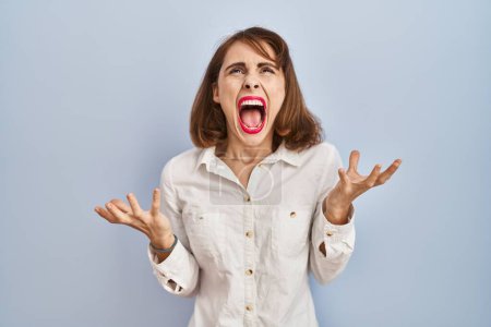 Photo for Young beautiful woman standing casual over blue background crazy and mad shouting and yelling with aggressive expression and arms raised. frustration concept. - Royalty Free Image