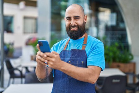 Photo for Young bald man waiter smiling confident using smartphone at coffee shop terrace - Royalty Free Image