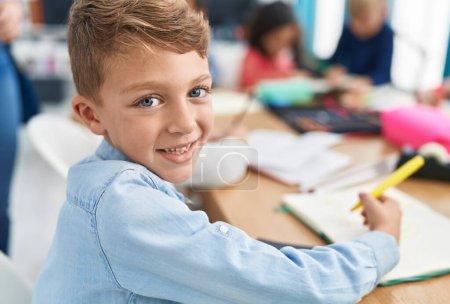Foto de Adorable caucásico niño estudiante dibujo en cuaderno de estudio en el aula - Imagen libre de derechos
