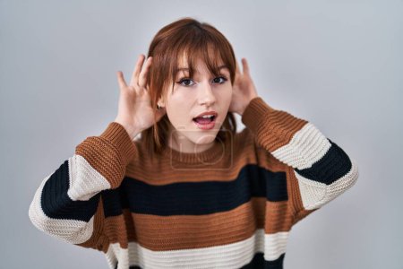 Photo for Young beautiful woman wearing striped sweater over isolated background trying to hear both hands on ear gesture, curious for gossip. hearing problem, deaf - Royalty Free Image
