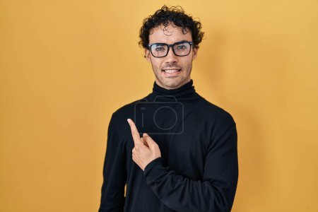 Téléchargez les photos : Homme hispanique debout sur fond jaune pointant de côté inquiet et nerveux avec index, expression inquiète et surprise - en image libre de droit