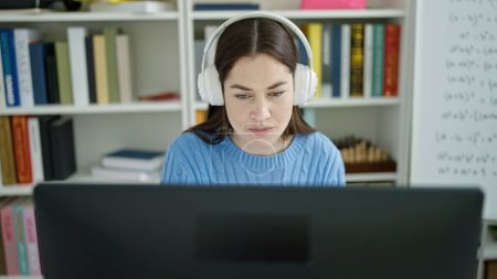 Téléchargez les photos : Jeune étudiante caucasienne utilisant ordinateur et écouteurs étudiant à l'université de la bibliothèque - en image libre de droit